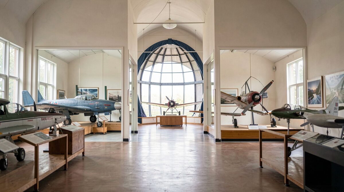 Intérieur d'un petit musée d'aviation : deux salles lumineuses avec maquettes d'avions et un globe de planetarium, cadrage frontal en lumière naturelle.
